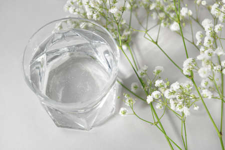 Glass of clean water and flowers on light backgroundの写真素材