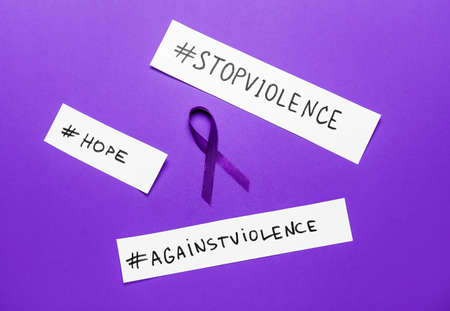 Violet ribbon with different hashtags on color background. Domestic violence concept