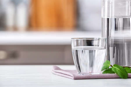 Glass and bottle of fresh cold water on table in kitchen