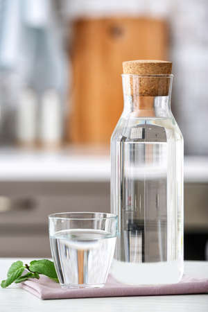 Glass and bottle of fresh cold water on table in kitchenの写真素材