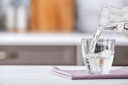 Pouring of fresh water into glass on table in kitchenの写真素材