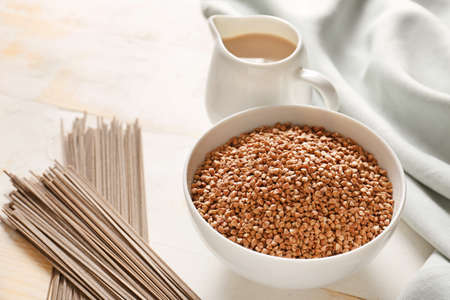 Bowl with raw buckwheat, pasta and milk on table