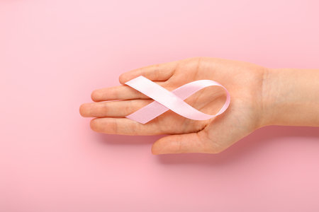 Female hand with pink ribbon on color background. Cancer awareness conceptの写真素材