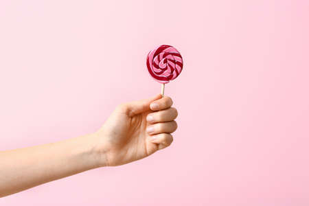 Female hand with sweet lollipop on color backgroundの写真素材