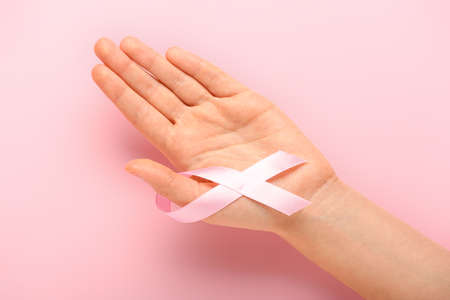 Female hand with pink ribbon on color background. Cancer awareness conceptの写真素材