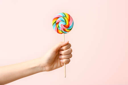 Female hand with sweet lollipop on color backgroundの写真素材