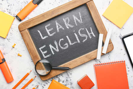 Chalkboard with text LEARN ENGLISH and stationery on light background