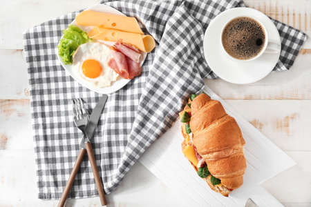 Tasty croissant sandwich with coffee and fried egg on tableの写真素材