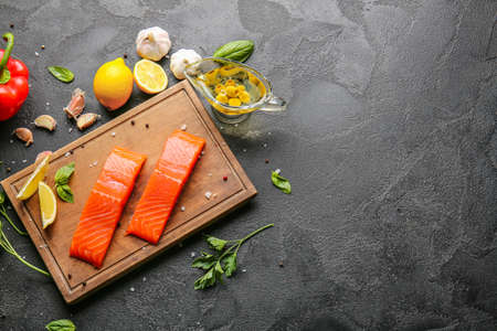 Raw salmon fillet with vegetables, oil and lemon on dark backgroundの写真素材