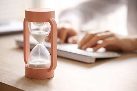 Hourglass and woman working on computer at table in officeの写真素材