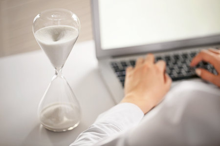 Hourglass and woman working on laptop at table in office