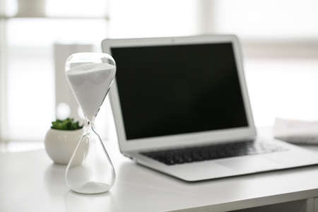 Hourglass with laptop on table in office. Time management conceptの写真素材