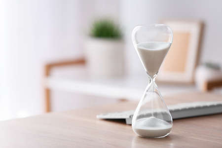 Hourglass with computer keyboard on table in office. Time management concept