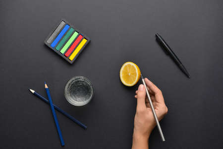 Female hand with stationery, lemon and glass of water on dark backgroundの写真素材