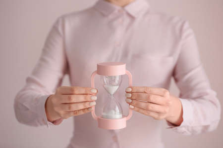 Woman with hourglass on light background, closeup. Time management concept