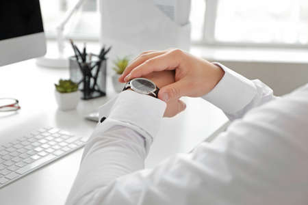 Young man looking at his watch in office, closeup