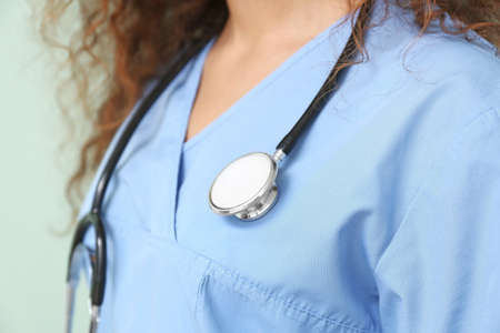 Young African-American nurse with stethoscope on color background, closeup