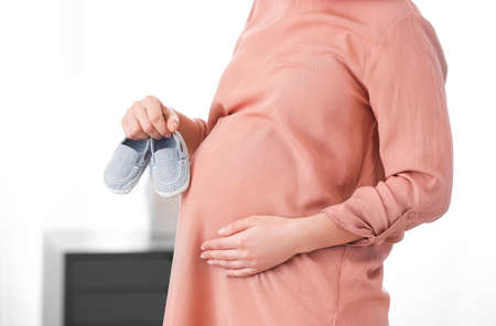 Pregnant woman with baby shoes at home, closeupの写真素材