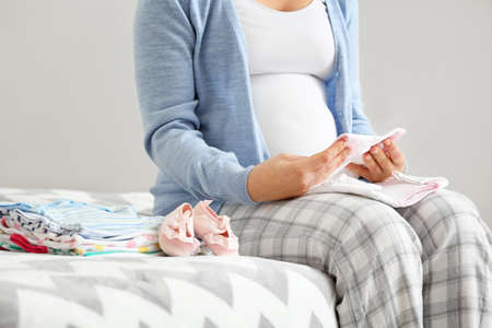 Pregnant woman with baby clothes in bedroom, closeupの写真素材