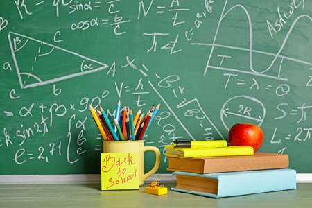 Set of school supplies and apple on table near blackboard