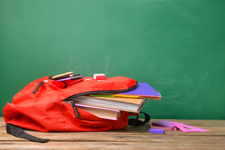 Backpack with school supplies on table near blackboard