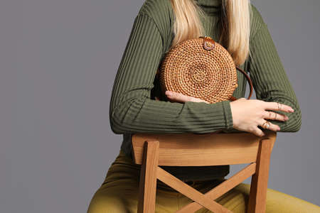 Young woman in warm sweater and with stylish bag on gray background
