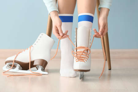 Young woman tying laces on ice skate shoes indoors