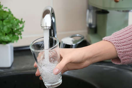 Woman filling glass with fresh water from kitchen faucetの写真素材