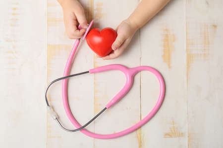 Child's hands with red heart and stethoscope on wooden background. Cardiology conceptの写真素材