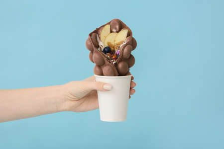 Female hand with delicious sweet bubble waffle on color backgroundの写真素材