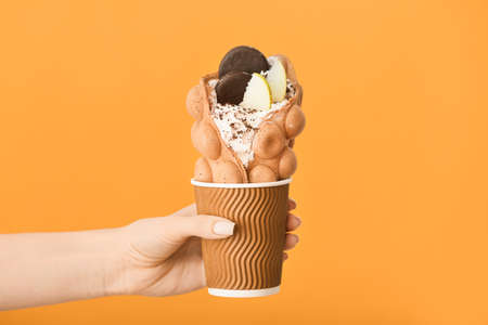 Female hand with delicious sweet bubble waffle on color background