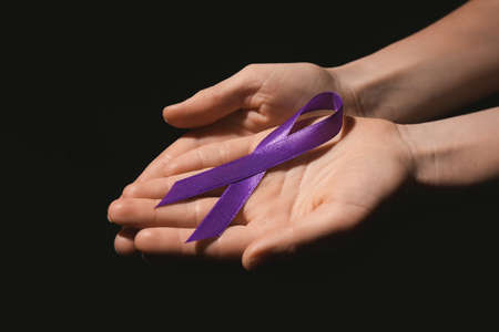 Female hands with violet ribbon on dark background. Domestic violence concept
