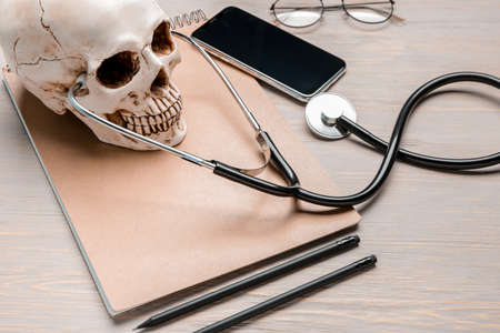 Stethoscope with human skull, notebook and mobile phone on wooden tableの写真素材