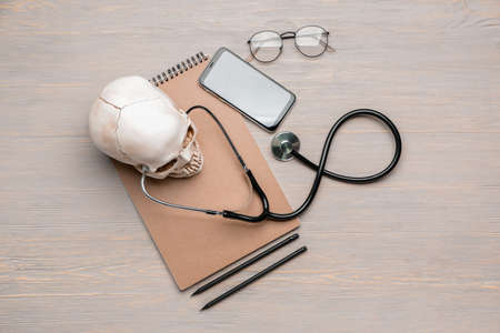 Stethoscope with human skull, notebook and mobile phone on wooden tableの写真素材