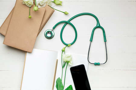 Stethoscope with notebooks and mobile phone on white wooden background