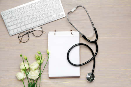 Stethoscope with notebook, computer keyboard and flowers on wooden backgroundの写真素材