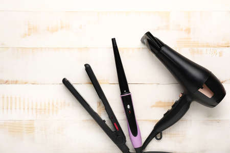 Modern hair dryer and irons on light wooden backgroundの写真素材