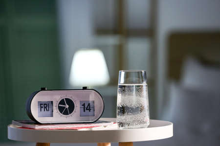 Glass of water and alarm clock on table in bedroom
