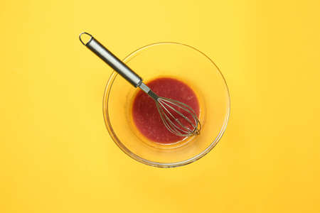 Dirty empty bowl with whisk on color background