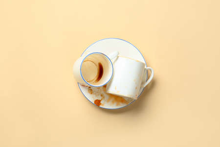 Dirty empty cups with plate on color background