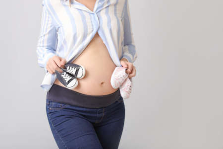 Beautiful pregnant woman with baby shoes on gray backgroundの写真素材