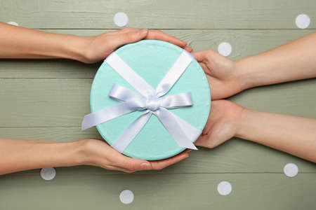 Female hands with beautiful gift box on color background