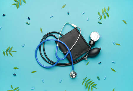 Stethoscope with sphygmomanometer and pills on color background