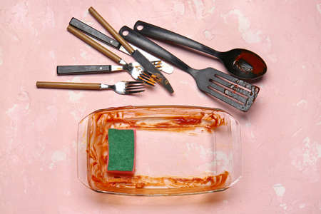 Dirty baking dish, cutlery and kitchen utensils on color background