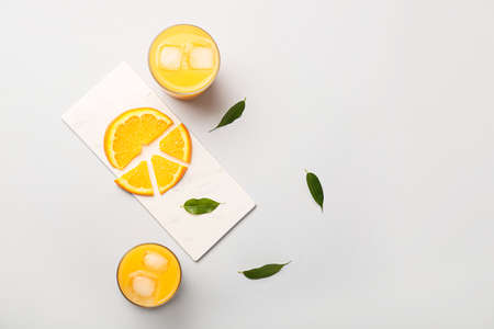 Glasses of fresh orange juice and fruit on light background