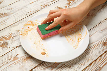 Woman washing dirty plate on light wooden backgroundの写真素材