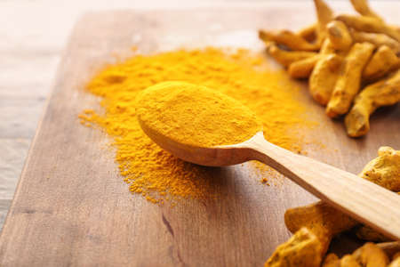 Spoon with aromatic turmeric on wooden board
