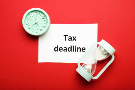 Paper sheet with text TAX DEADLINE, clock and hourglass on color background