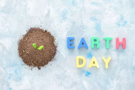 Heap of soil with plant and text EARTH DAY on color backgroundの写真素材