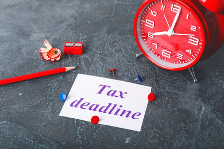 Paper with text TAX DEADLINE, alarm clock and pencil on dark table